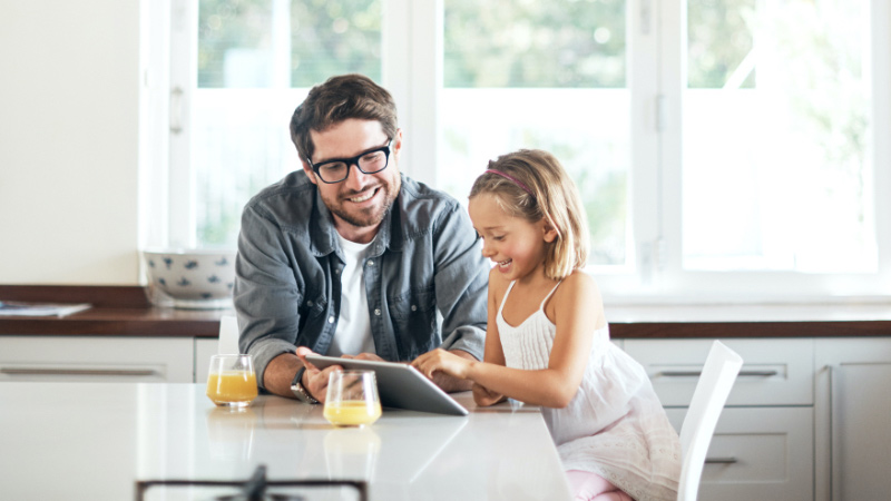 Dad watching daughter use a tablet